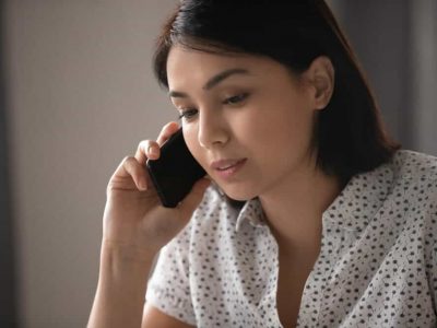 Close up of a young, pensive Asian woman listening to someone talking to her on her phone