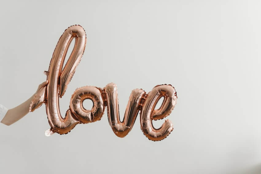 find lasting love - person holding a rose gold balloon made of the letters spelling love