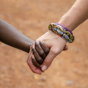 Close up of a white adult's hand holding the smaller hand of a black child
