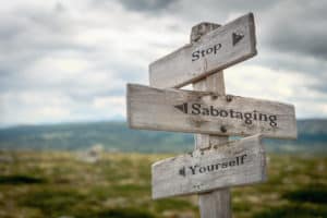 Stop sabotaging yourself text engraved on an old wooden signpost.