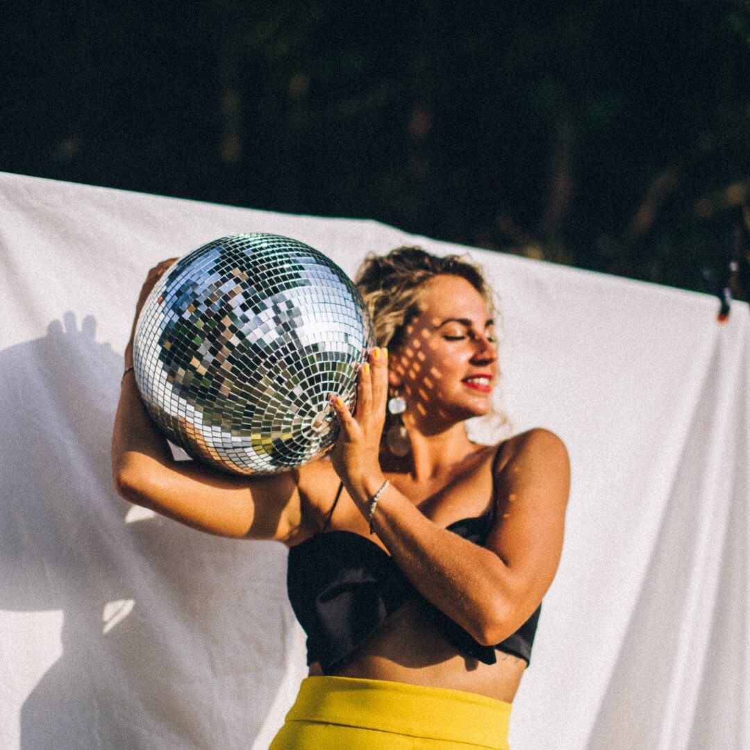 woman with blonde hair, eyes closed, holding a disco ball