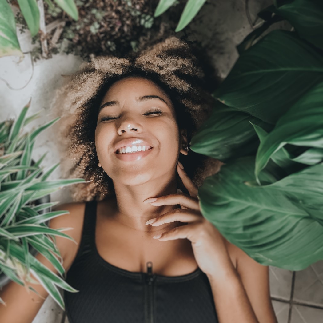 Woman laying and smiling among large leaves to represent being at ease