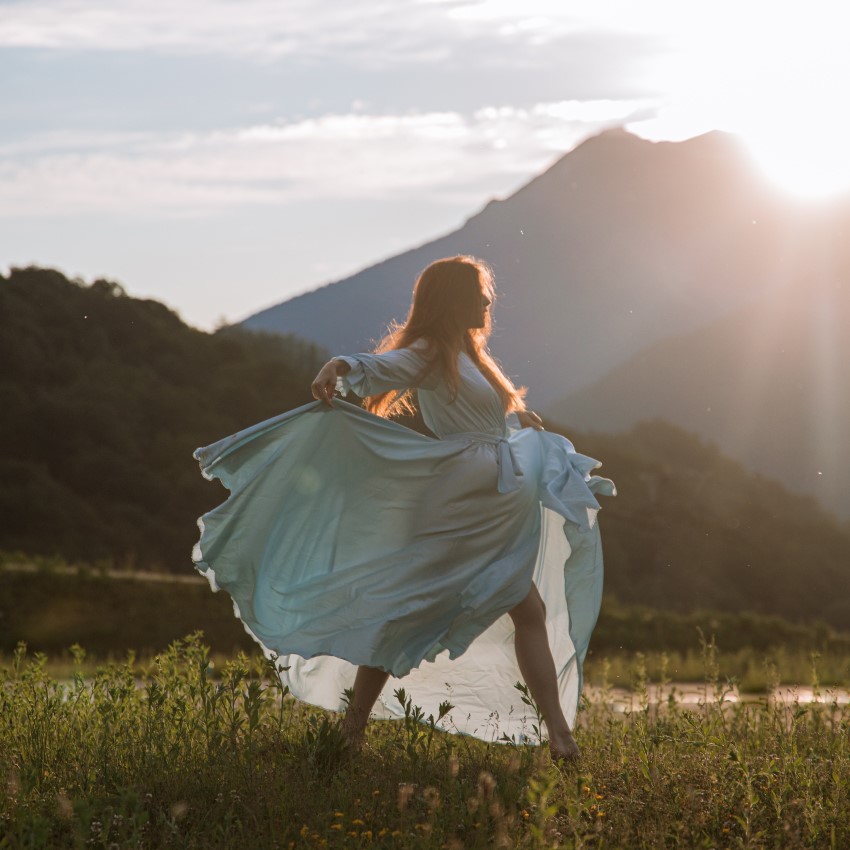 woman in a blue dress in a field with a mountain in the back