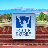 Focus on the Family welcome sign at the main entrance, showing Pike's Peak in the background on a clear summer day